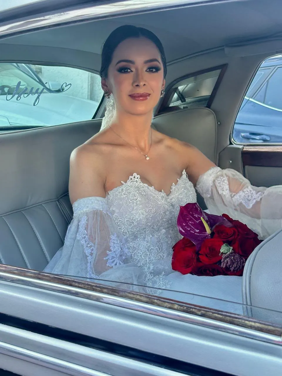 Novia sonriendo con su ramo dentro de un auto clásico