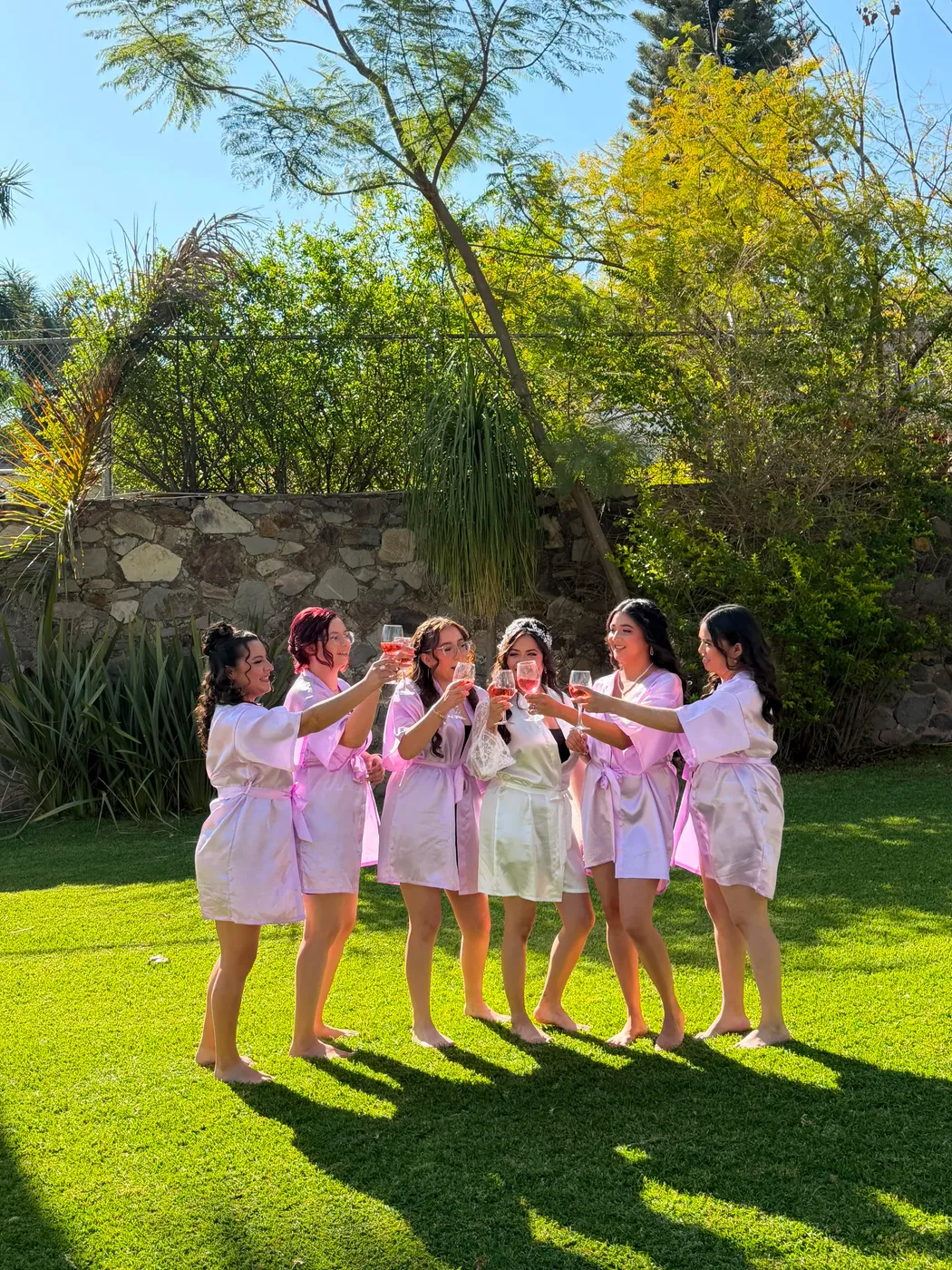 Novia brindando con sus damas en batas rosas en el jardín